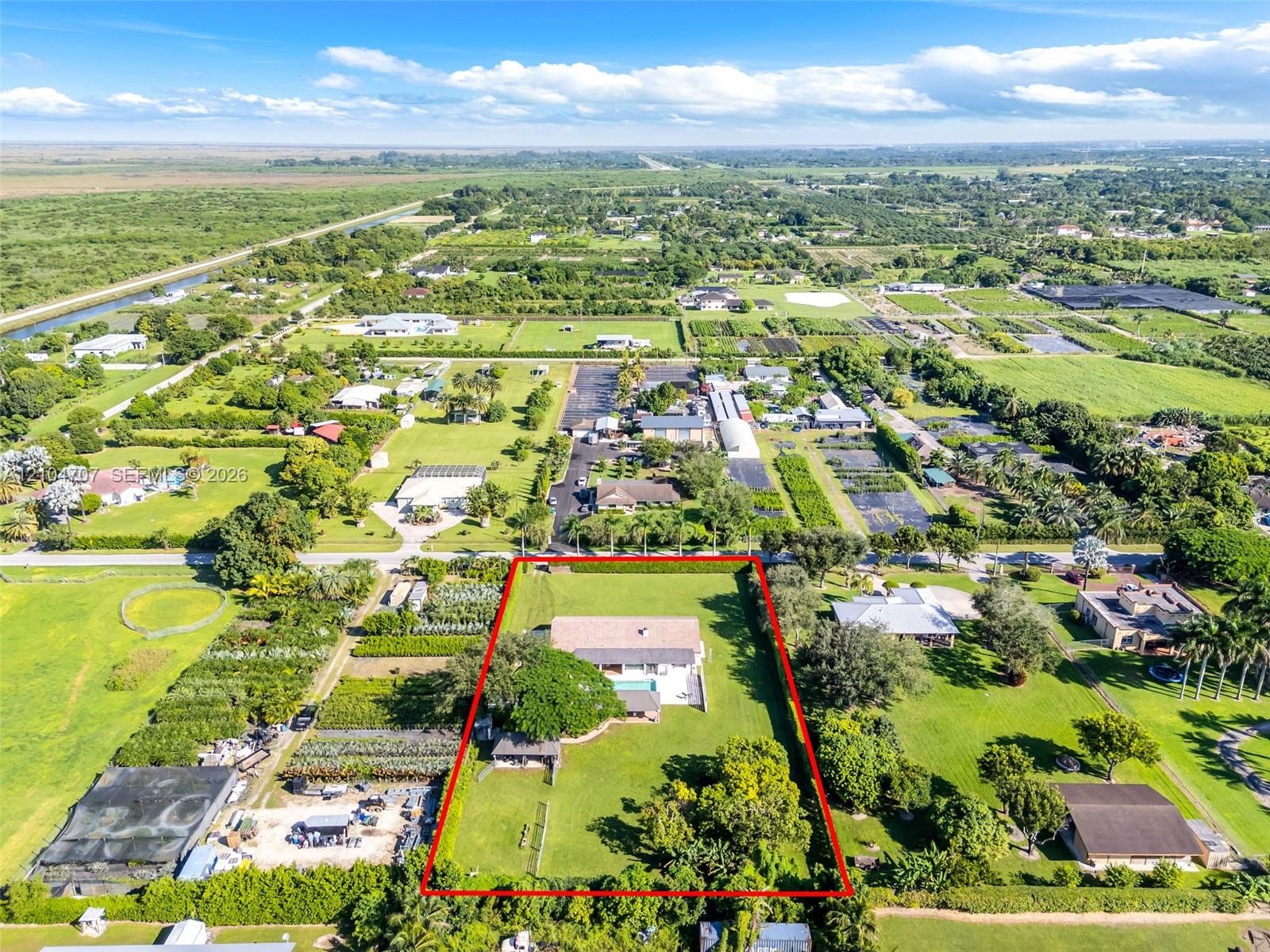 Aerial perspective of a sprawling property featuring a multi-pitched roof residence, a rectangular swimming pool, extensive manicured grounds, mature 