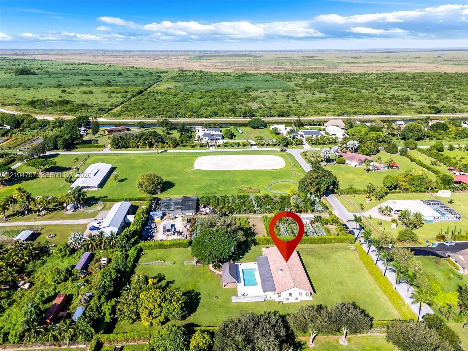 Aerial perspective of a property featuring a tiled roof, attached garage, swimming pool, and expansive grounds with mature perimeter landscaping