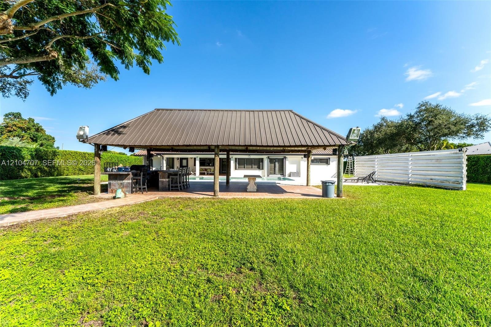 Expansive backyard featuring a manicured lawn, perimeter privacy hedging, and mature palm trees