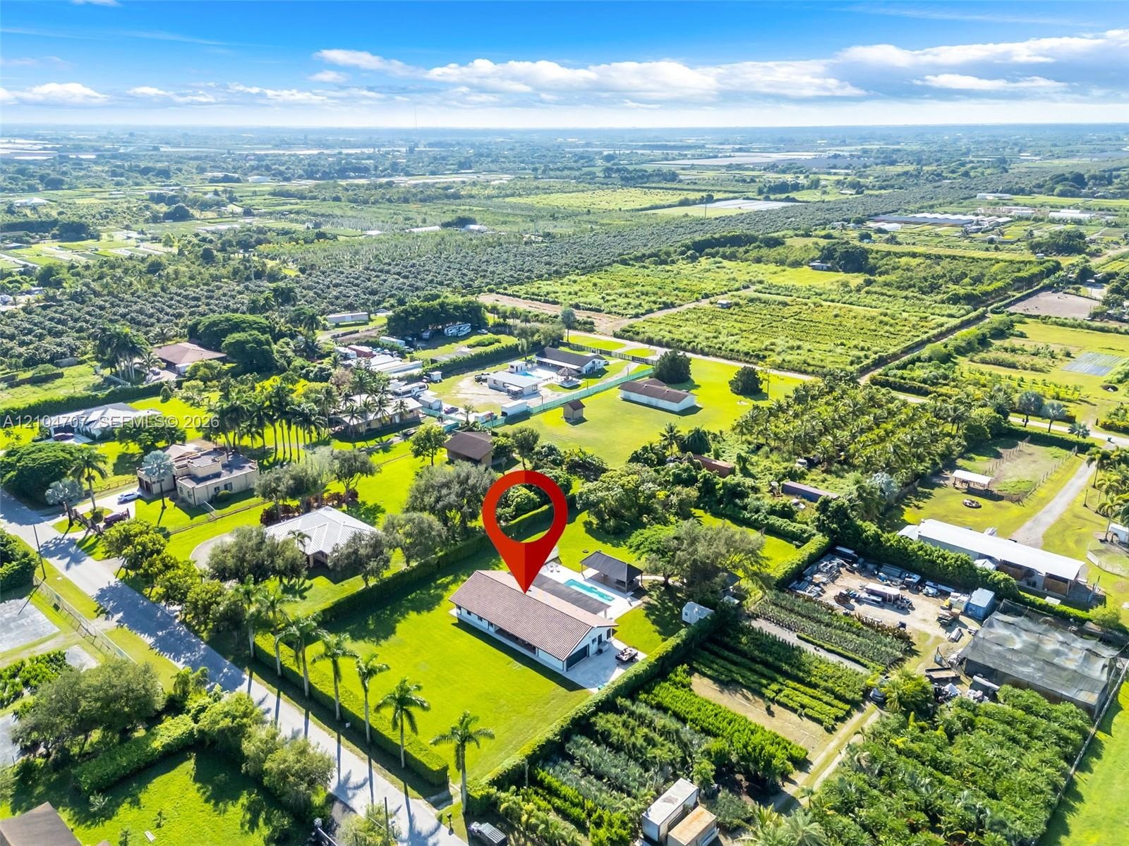 Aerial perspective of a sprawling lot featuring a rectangular swimming pool, concrete patio, extensive lawn, and mature perimeter landscaping