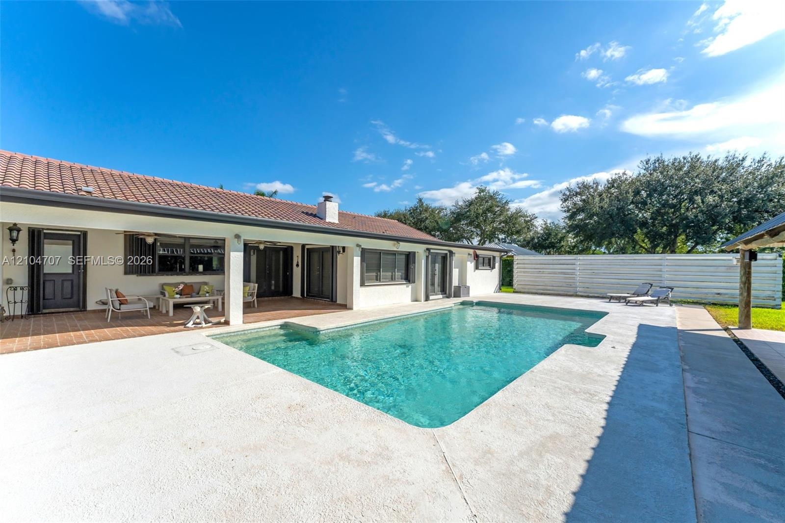 In-ground swimming pool featuring a concrete deck, covered patio, tile roof, and privacy fencing