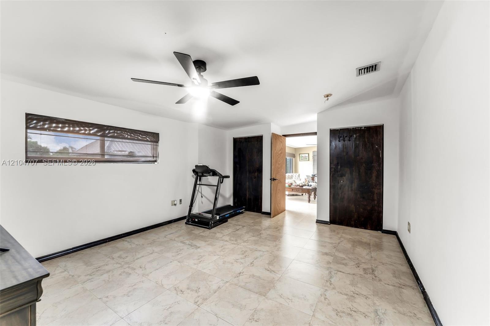 Room featuring large-format stone-style tile flooring, dark wood-finish interior doors, and a ceiling fan with integrated lighting