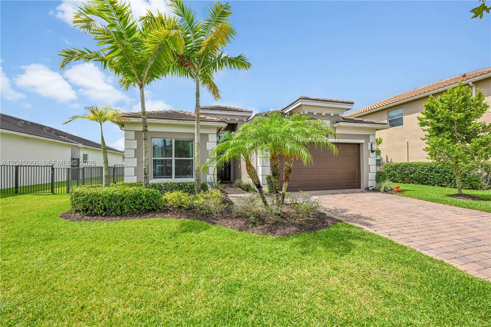 Stucco exterior with multi-level rooflines, paver driveway, single-car garage, and landscaped front yard with palm trees