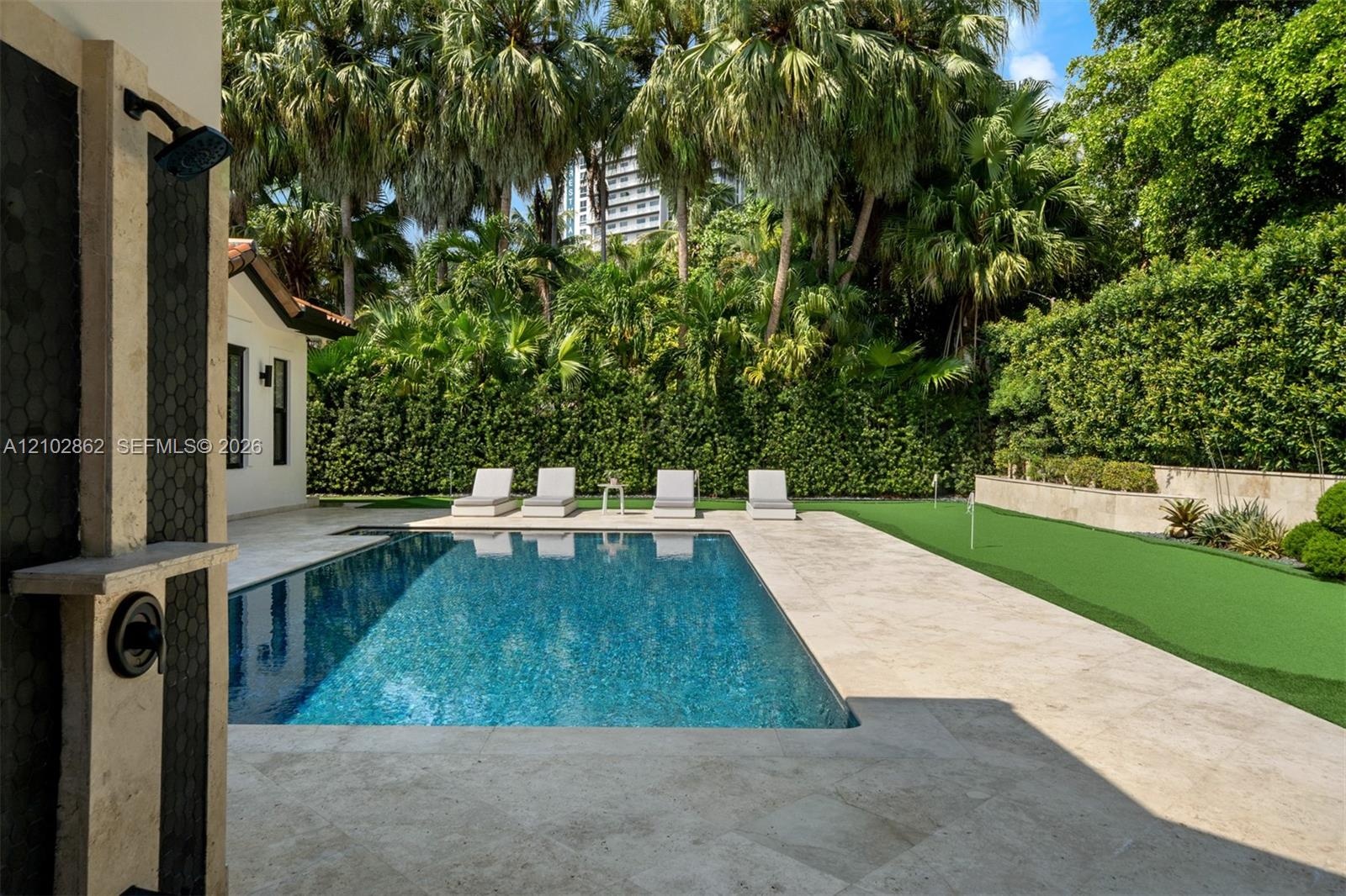 Outdoor kitchen featuring a stainless steel grill, a built-in refrigerator, stone-finish countertops, and a stone-tiled patio bordered by mature priva