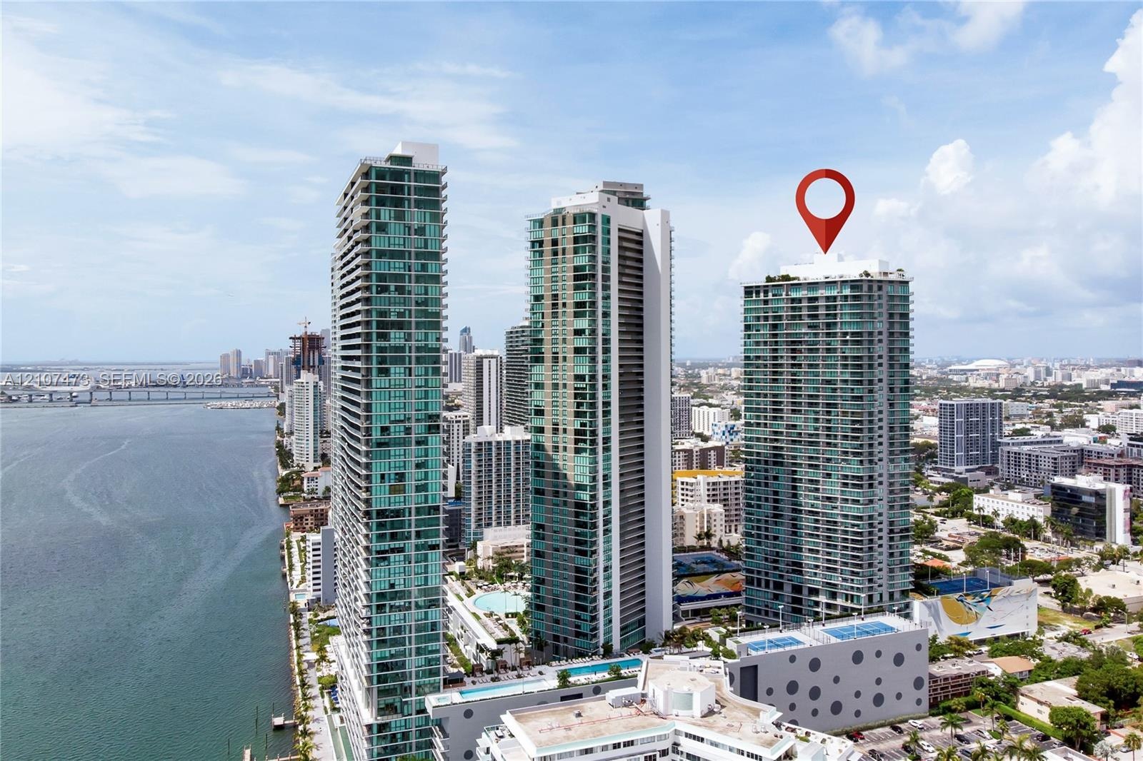 High-rise glass facade condominium tower featuring private balconies, integrated parking structure, and rooftop amenity deck, situated within a coasta