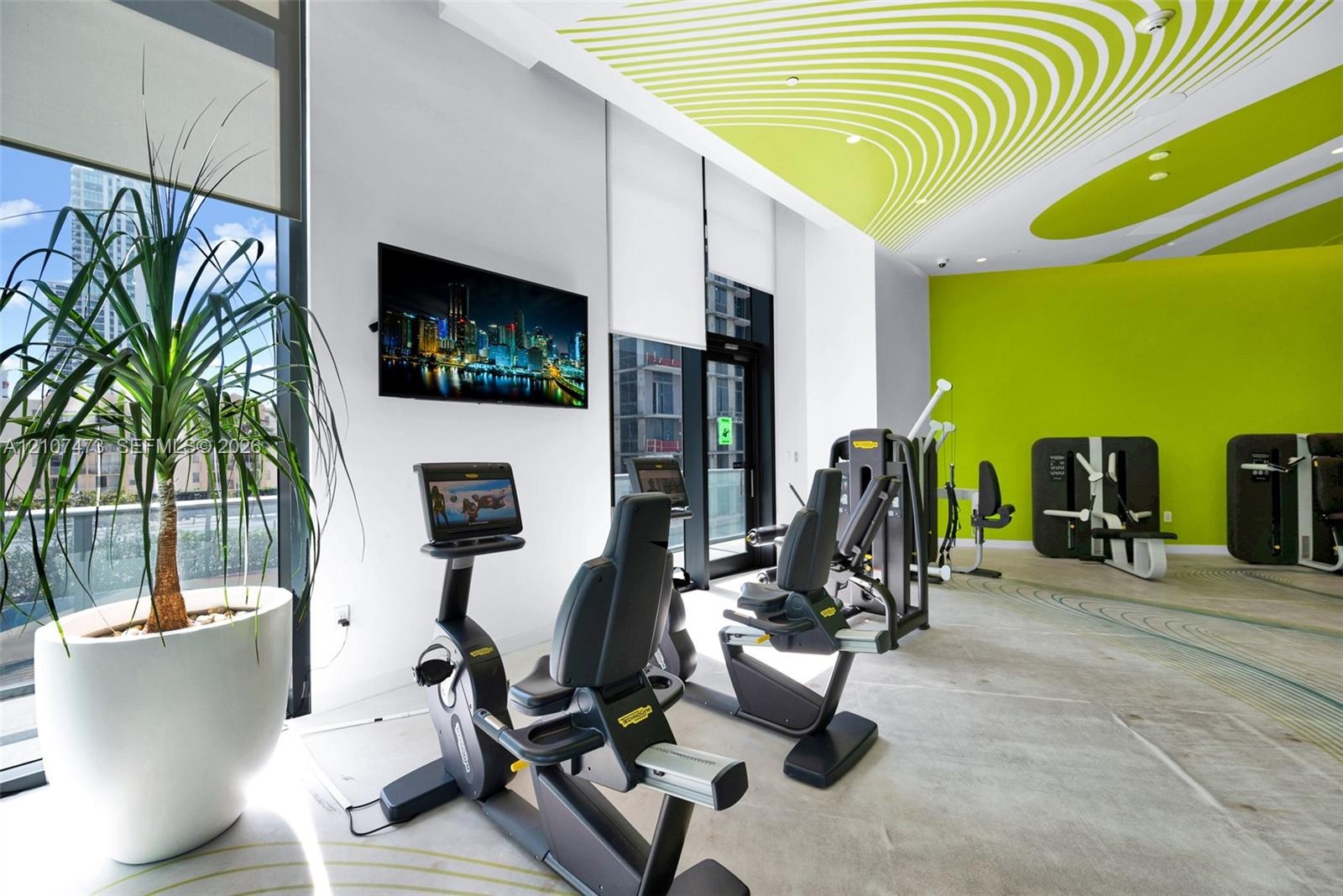 Fitness facility featuring floor-to-ceiling windows, high ceilings with decorative acoustic panels, polished concrete flooring, and wall-mounted telev