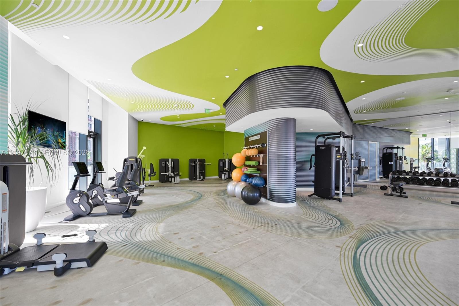Fitness center featuring expansive floor-to-ceiling windows, high-contrast patterned ceiling, curved corrugated-metal structural accents, and large-fo