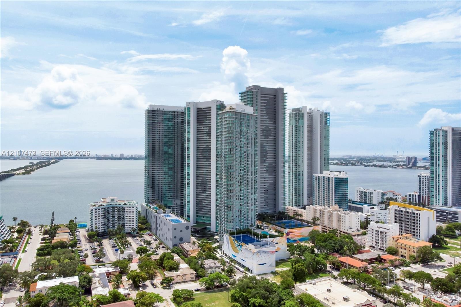 High-rise glass and concrete residential towers situated on a waterfront peninsula featuring multi-level podium parking structures, rooftop recreation