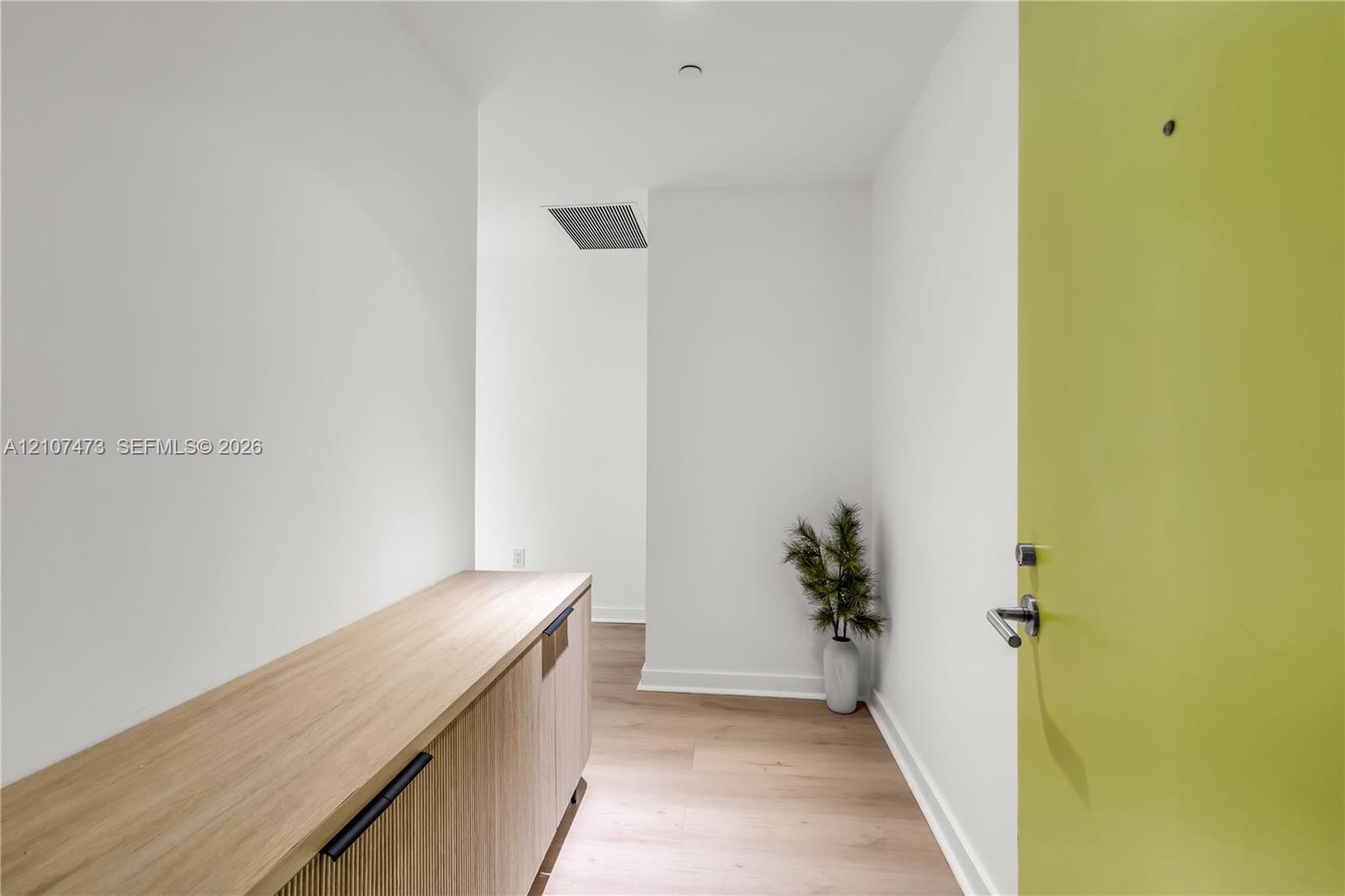 Entryway featuring a light-tone door with a modern lever handle, built-in wooden cabinetry with matte black hardware, and light wood-finish flooring