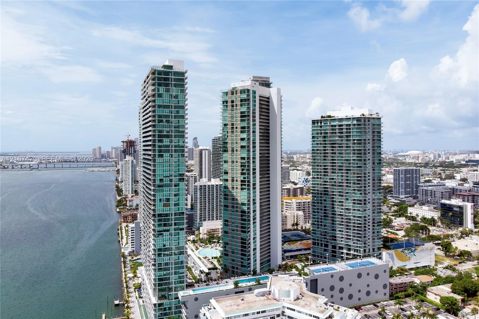 High-rise towers featuring glass facades, multi-level podium structures, swimming pools, and concrete parking facilities, situated on the waterfront