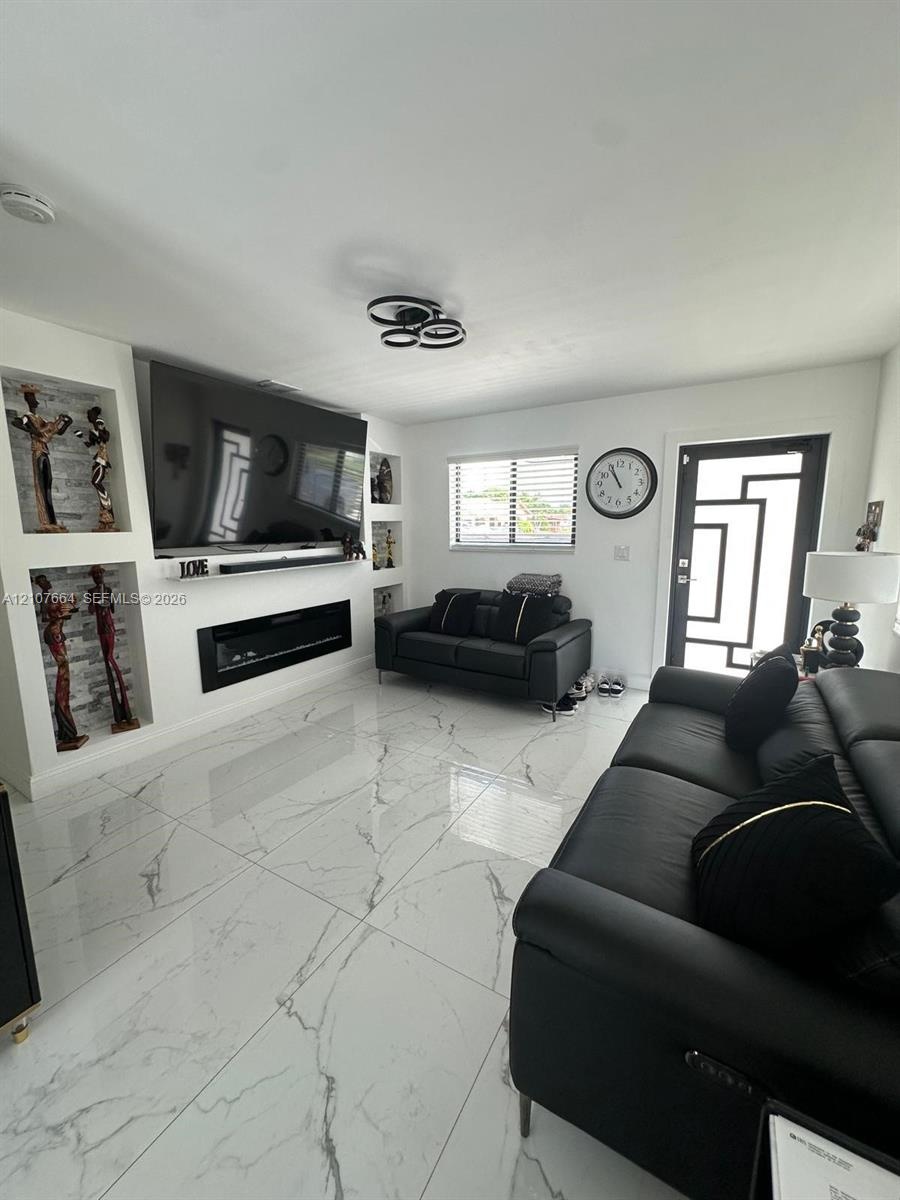 Large-format porcelain tile flooring, built-in wall niches, linear electric fireplace, modern flush-mount multi-ring ceiling lighting, and geometric-p