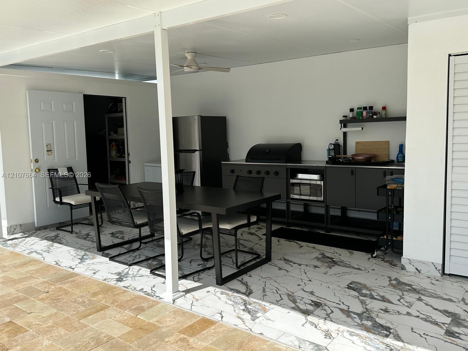 Covered outdoor kitchen area featuring high-contrast tile flooring, matte black cabinetry, a built-in grill, and an integrated ceiling fan