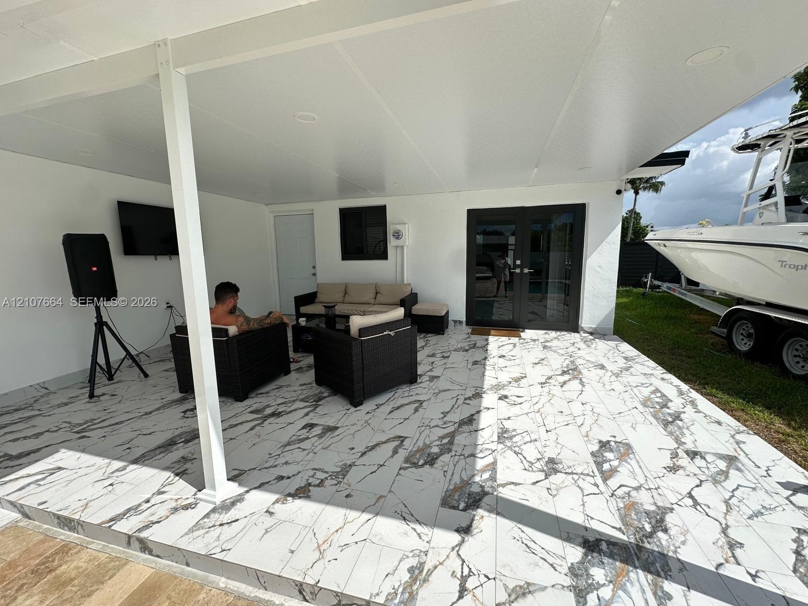 Covered outdoor patio featuring large-format stone-look tile flooring, recessed ceiling lighting, and double glass-paned doors