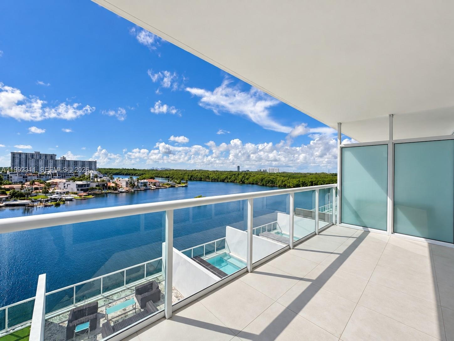 Covered balcony featuring large-format porcelain tile flooring, glass panel railings, and frosted privacy partitions, overlooking a waterfront skyline