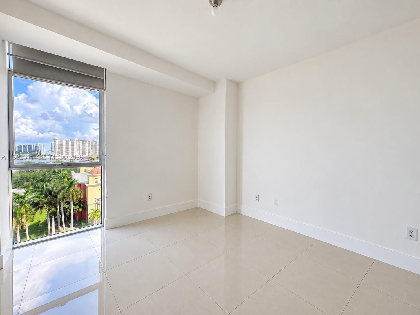 Neutral-toned interior featuring large-format tile flooring, multi-panel closet doors, floor-to-ceiling window, and exterior water and cityscape scene