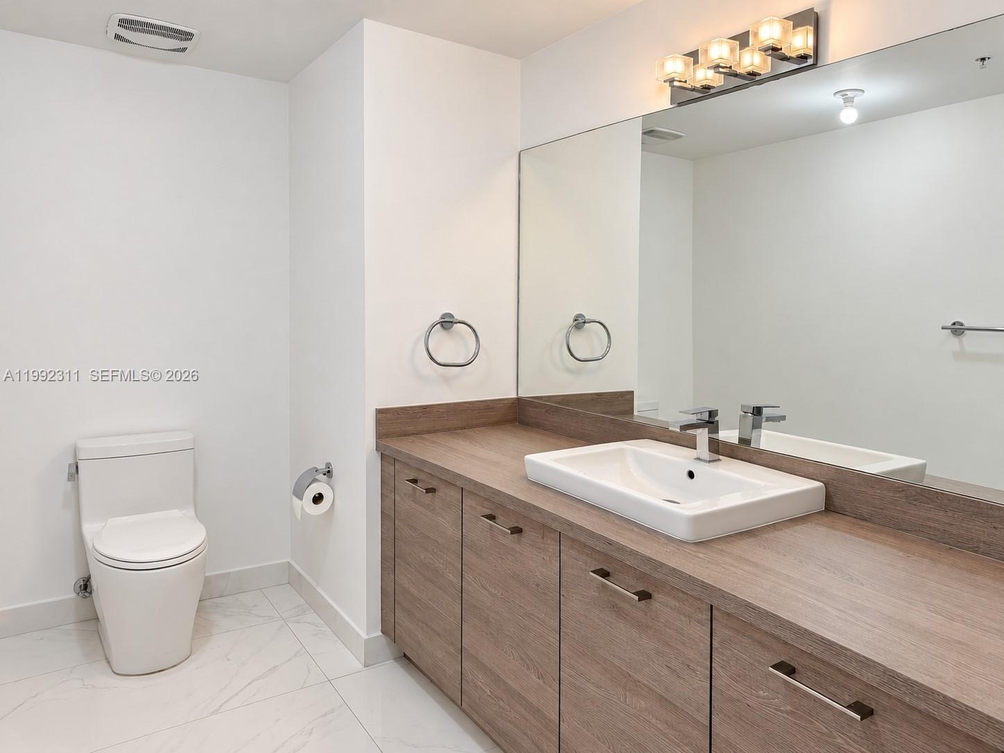 Floating wood-finish double vanity with rectangular vessel sinks, soaking tub, glass-enclosed walk-in shower with stone tile flooring, and large-forma