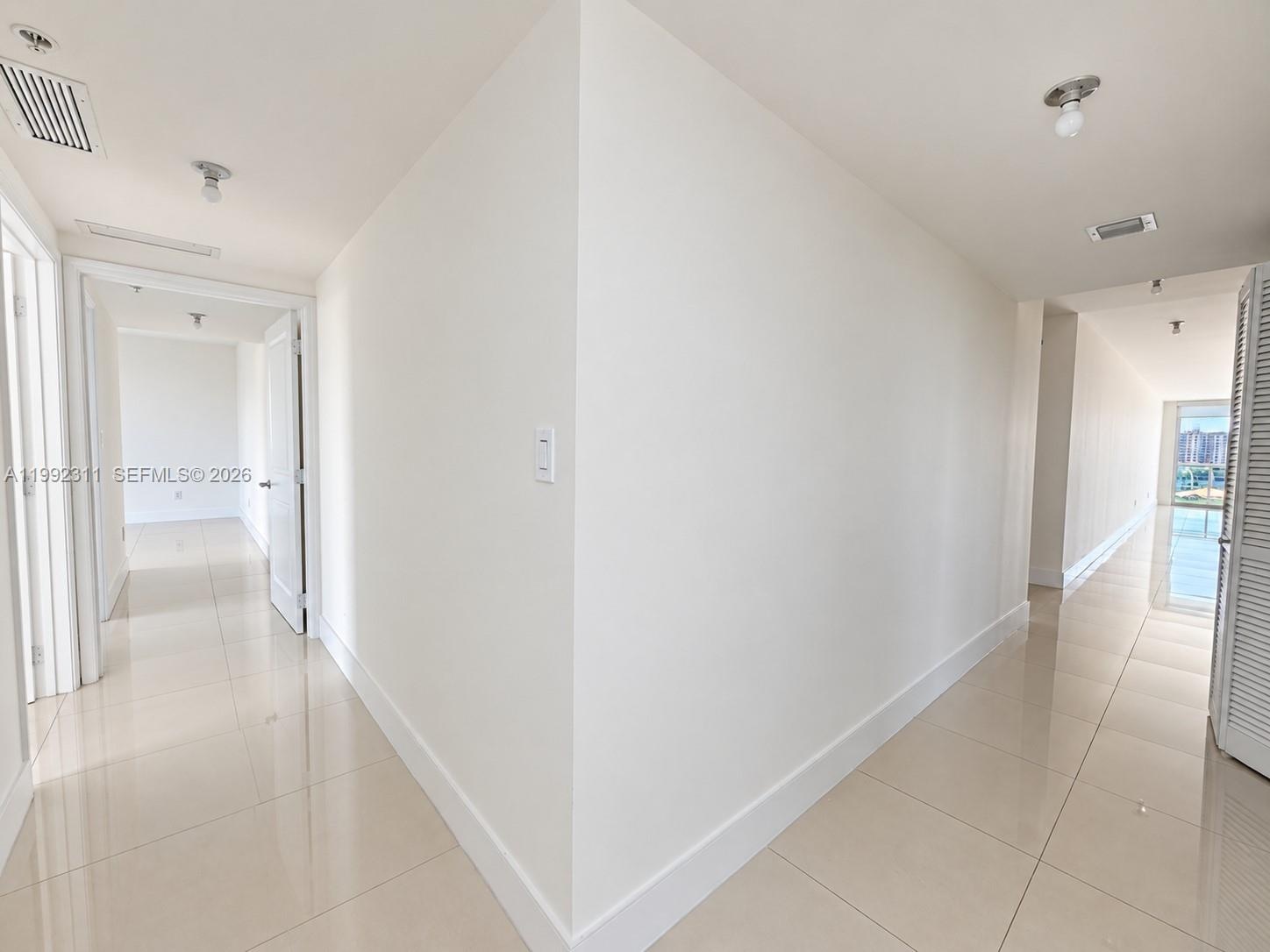 Room interior featuring polished tile flooring, neutral walls, ceiling-mounted lighting, and oversized windows with roller shades