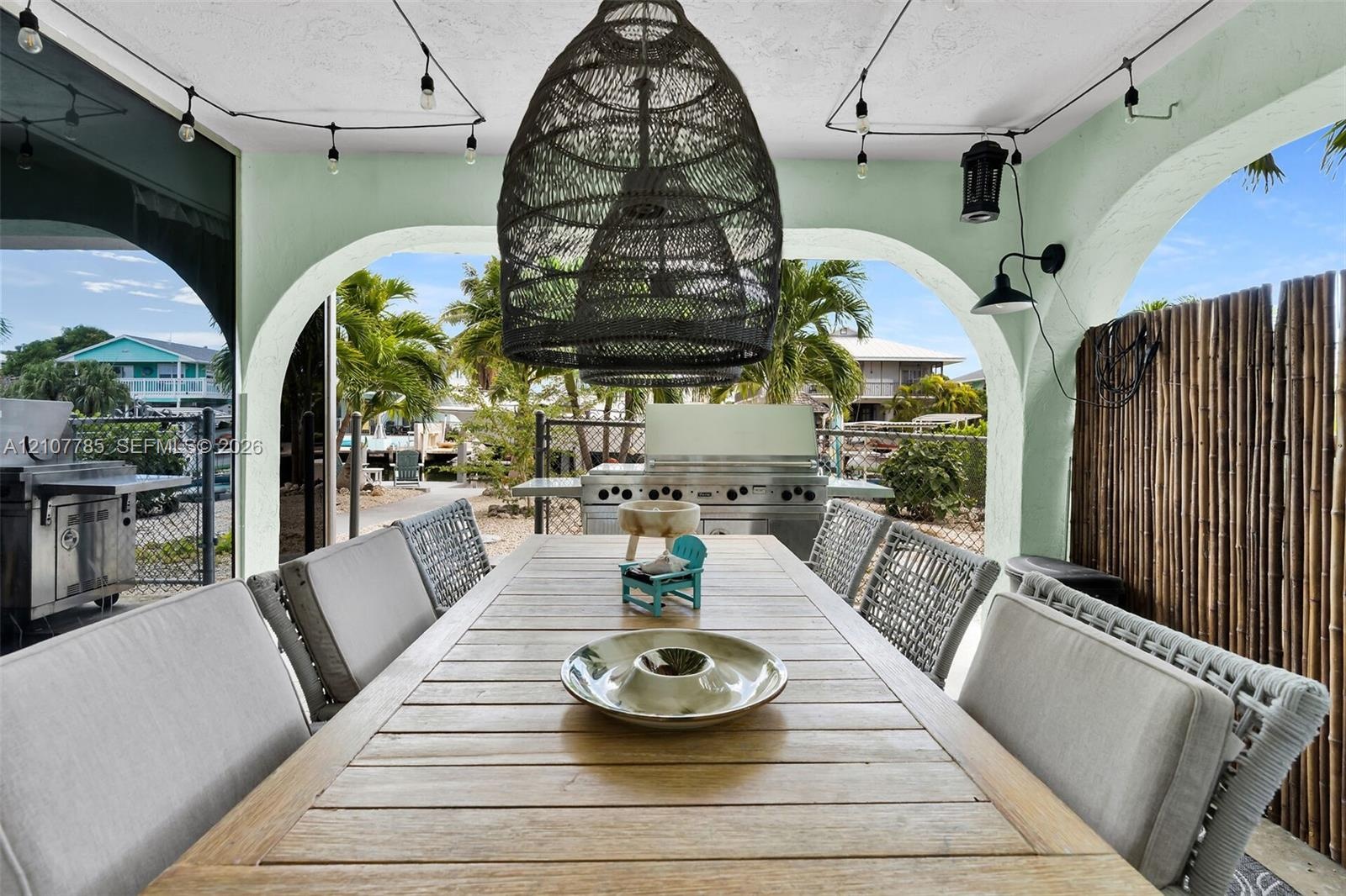 Covered outdoor living space featuring arched structural openings, built-in stainless steel grill, woven pendant light fixture, and mounted exterior w