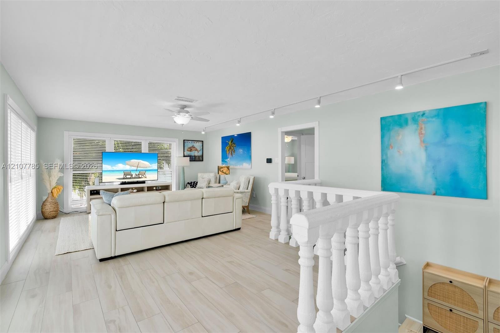 Open-concept room featuring wood-finish flooring, white traditional balustrade railing, track lighting, and ceiling fan