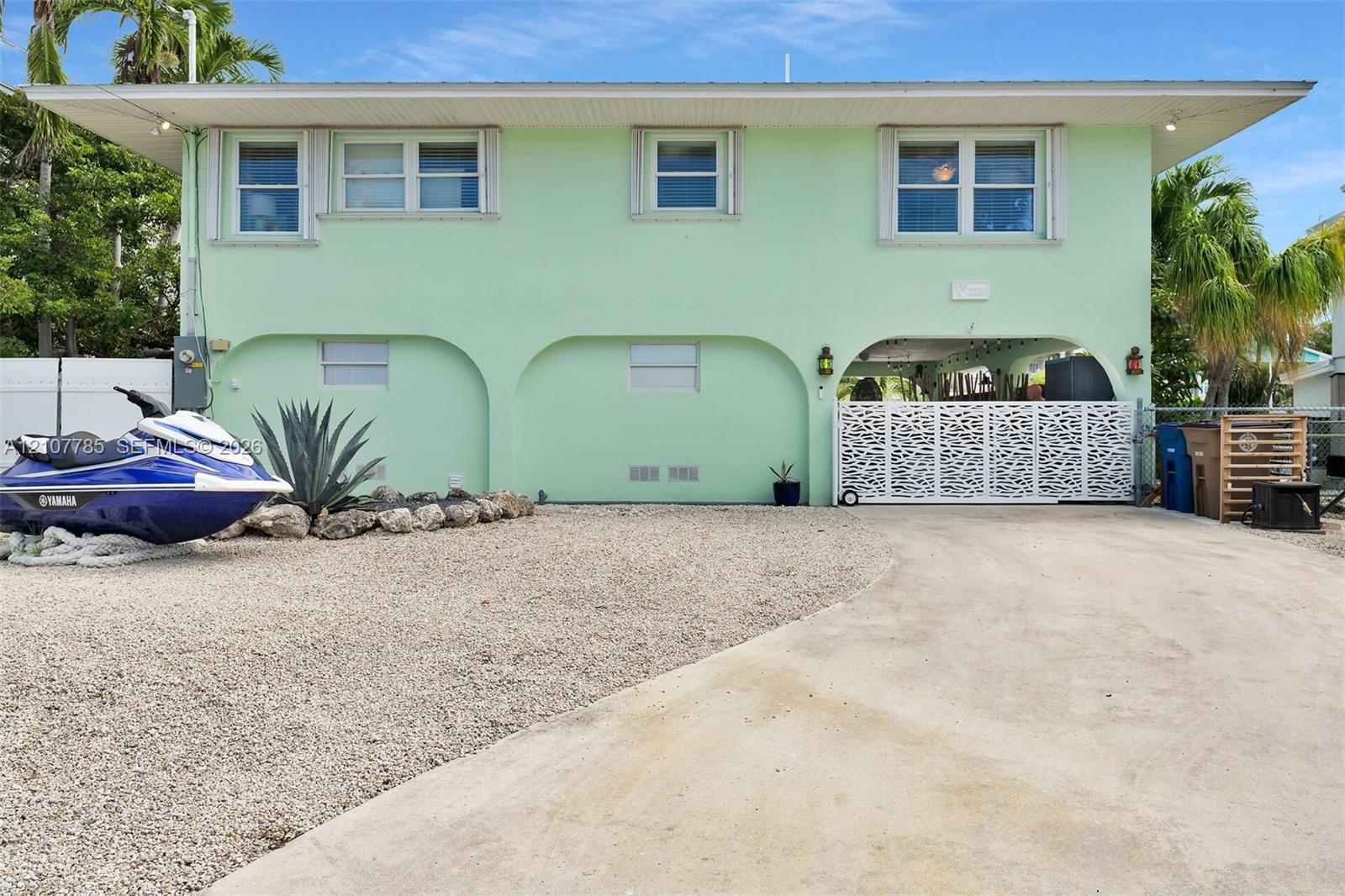 Two-story residence featuring architectural arched structural supports, a decorative metal privacy gate, concrete driveway, and low-maintenance gravel