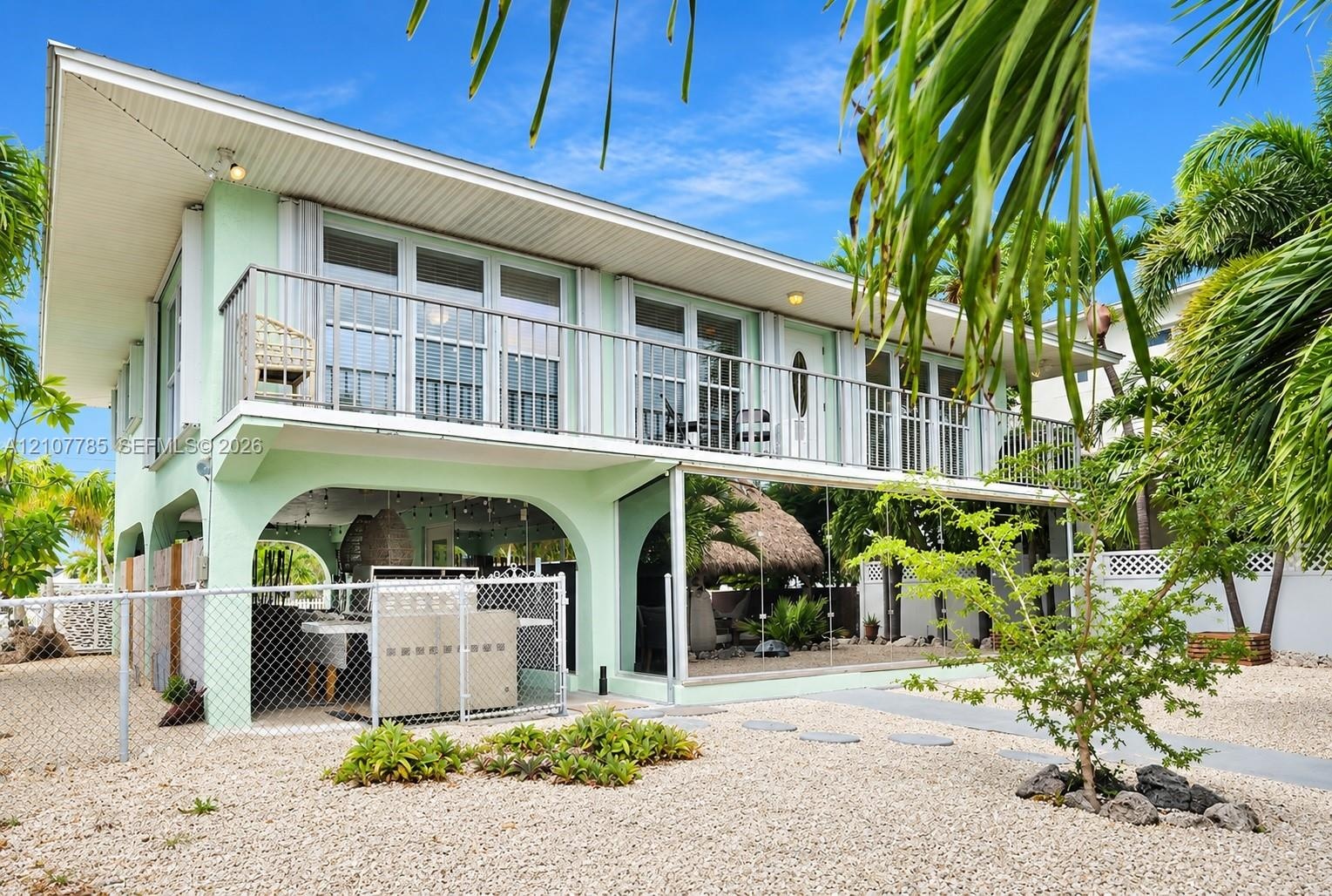 Elevated exterior featuring a second-story balcony with metal railing, ground-level covered patio with arched masonry, and exterior staircase