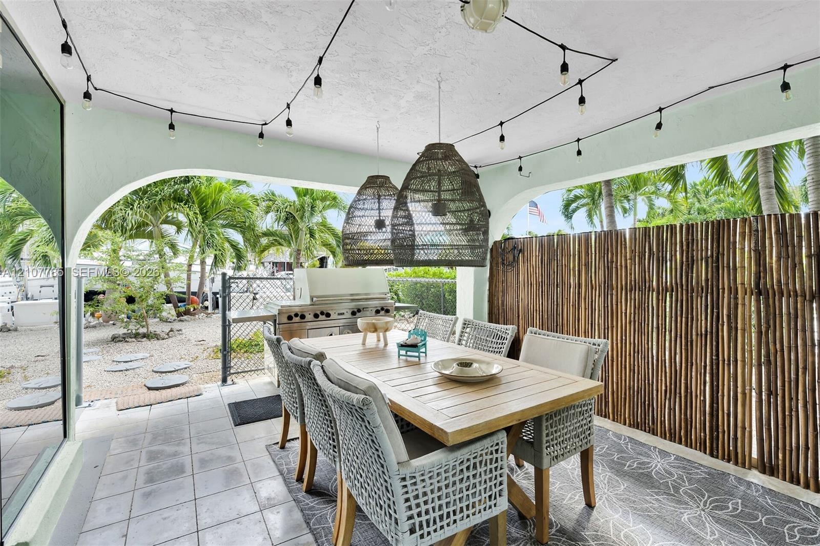 Covered patio featuring ceramic tile flooring, built-in stainless steel outdoor kitchen, arched architectural detailing, and decorative woven pendant 