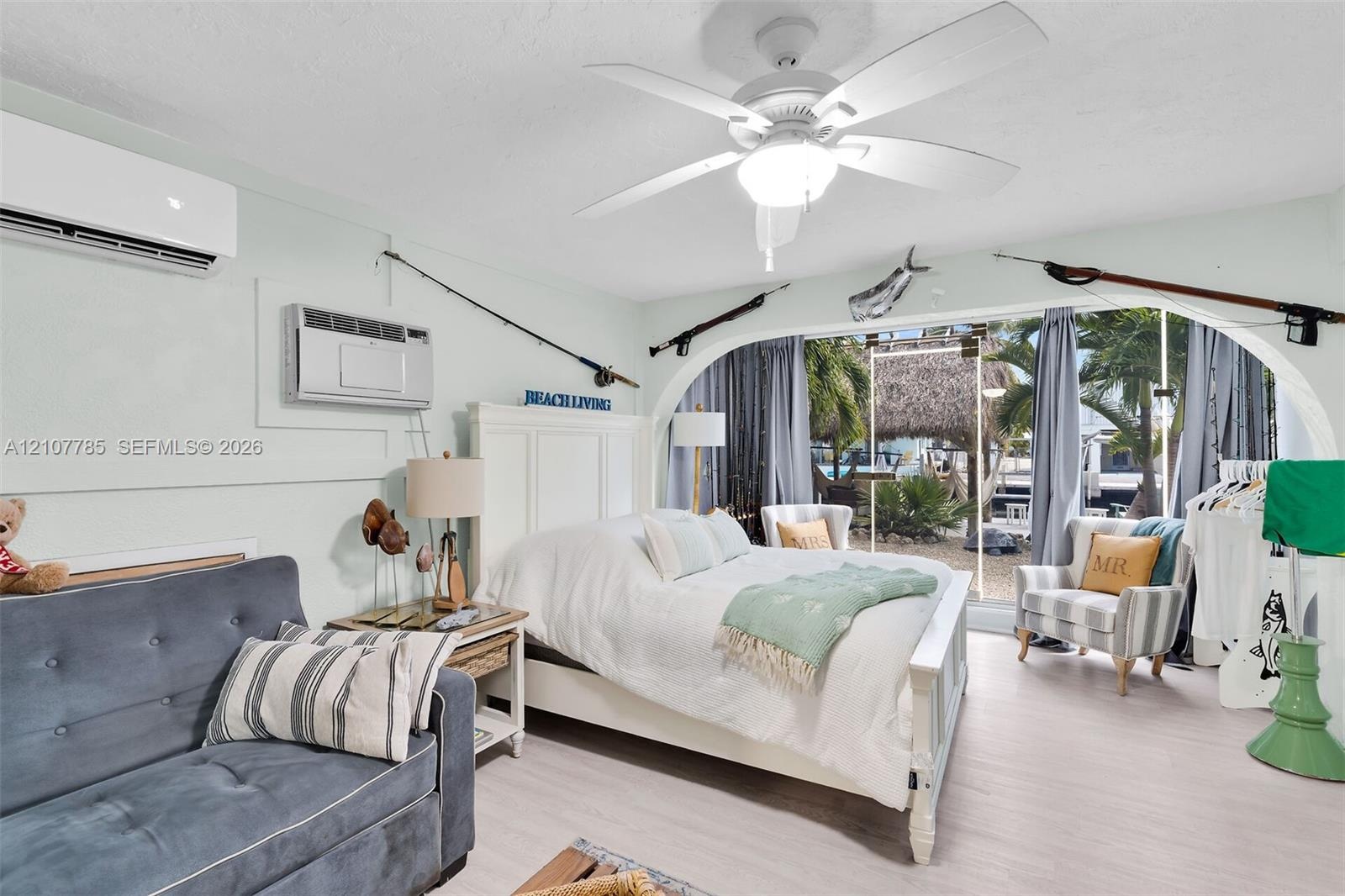 Light-toned wood-finish flooring, wall-mounted mini-split HVAC unit, ceiling fan with integrated lighting, and an arched glass entryway