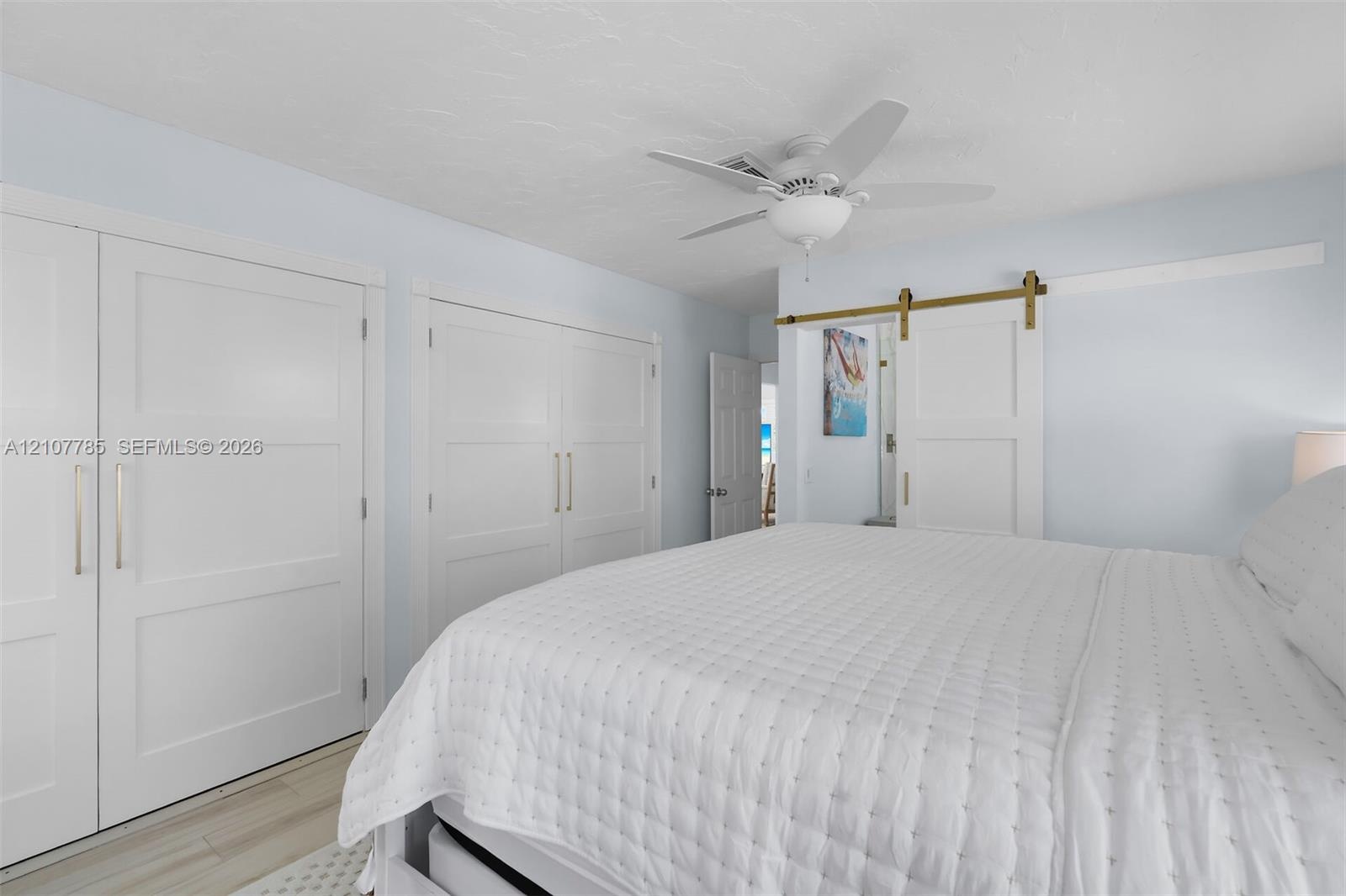 Dual closets featuring shaker-style doors with metallic hardware, sliding barn door with brass track, and ceiling fan with integrated light fixture