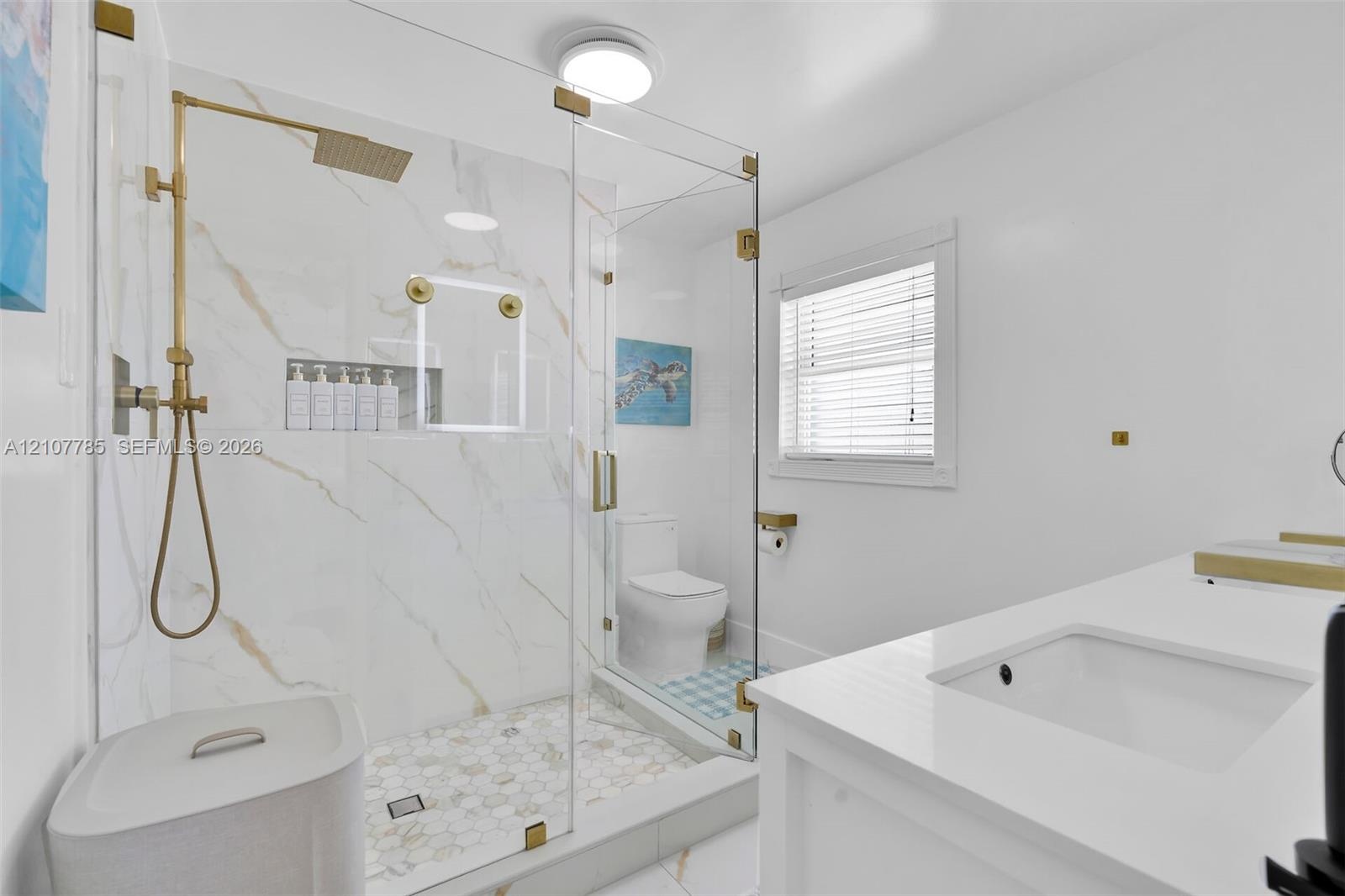 Walk-in shower with gold-tone hardware, a built-in recessed niche, stone-finish wall tile, a hexagonal tile floor, and a frameless glass enclosure