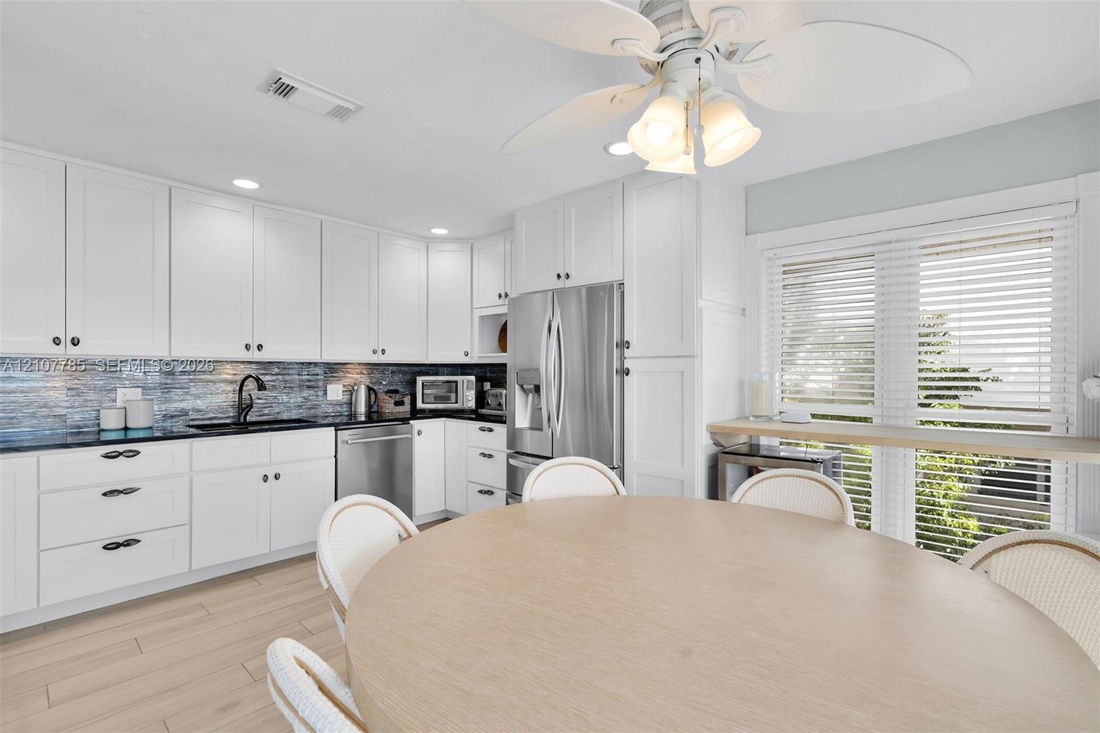 Kitchen featuring white shaker-style cabinetry, dark stone countertops, blue glass tile backsplash, stainless steel appliances, and wood-finish floori