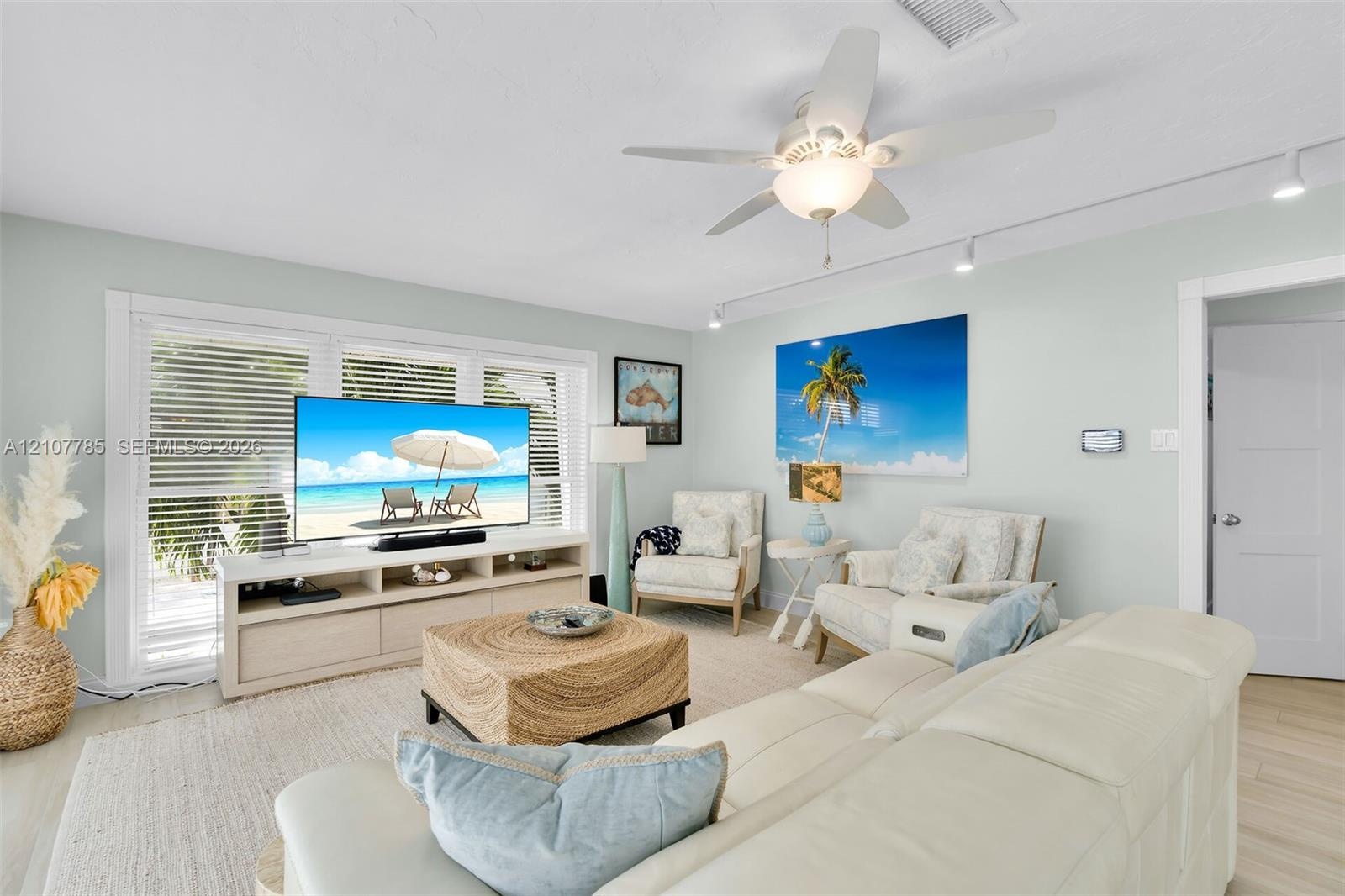 Living area featuring light-toned wood-finish flooring, recessed track lighting, a ceiling fan with integrated light fixture, and windows equipped wit