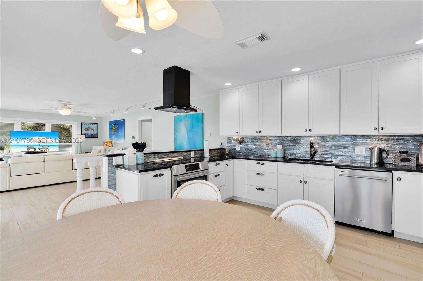 Kitchen featuring white cabinetry, dark countertops, a textured tile backsplash, a stainless steel dishwasher, and a matte black wall-mounted range ho