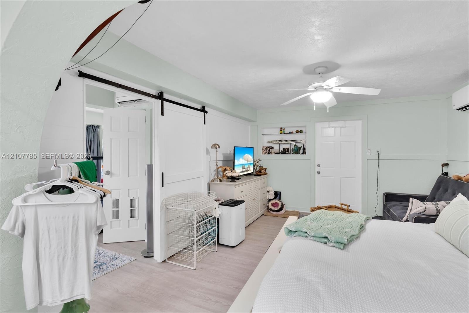 Room featuring wood-finish flooring, a sliding white barn door, a recessed wall niche with glass shelving, a multi-paneled door, and an attached ceili