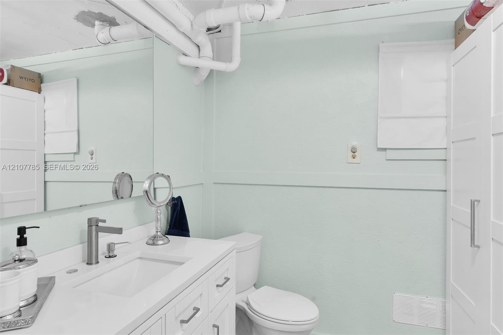 Bathroom featuring a white vanity with an integrated sink, polished metal faucet, full-width wall mirror, and built-in storage cabinetry
