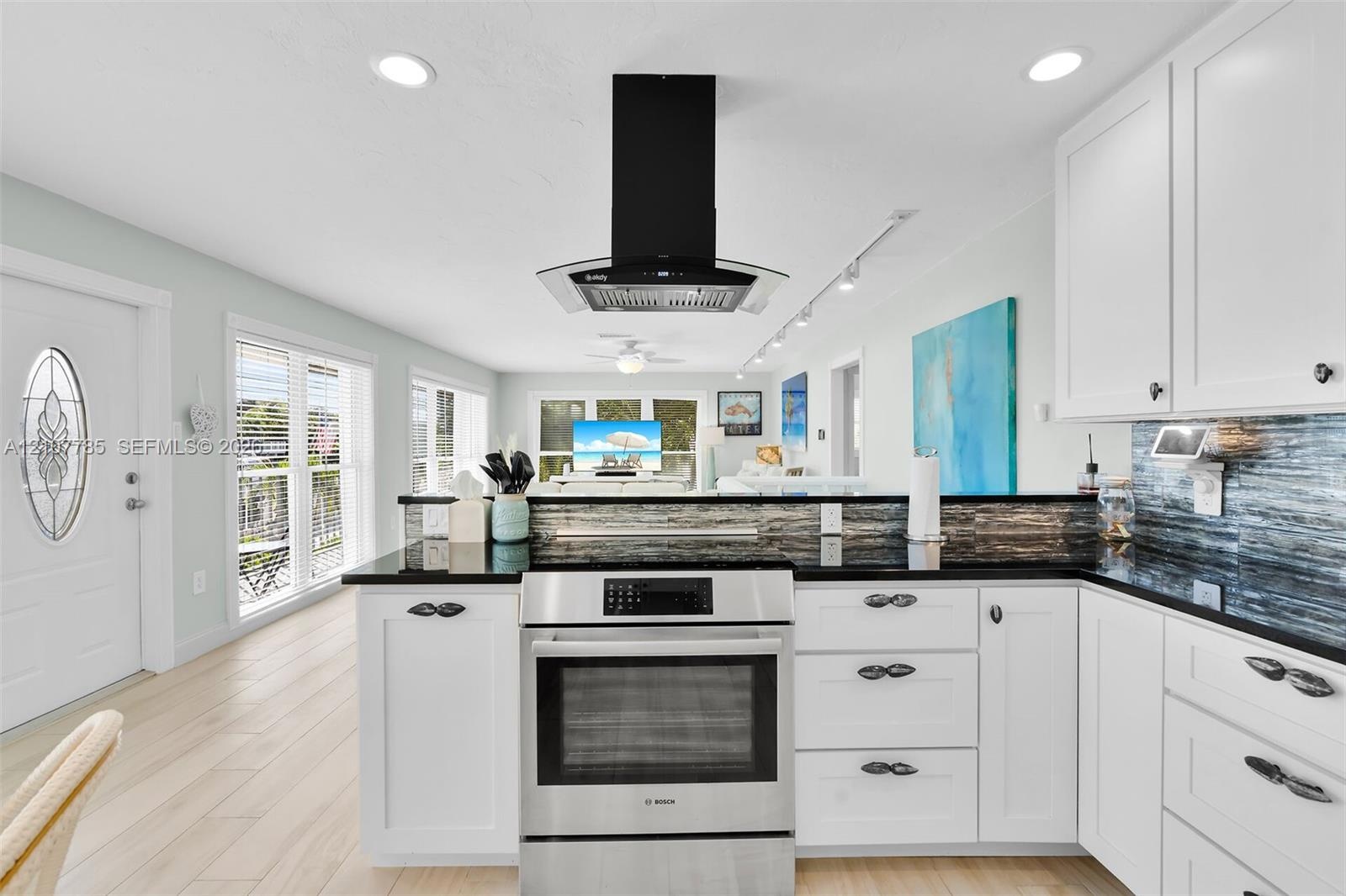 Kitchen featuring white cabinetry, dark countertops, a tiled backsplash, stainless steel oven, and a black chimney-style range hood
