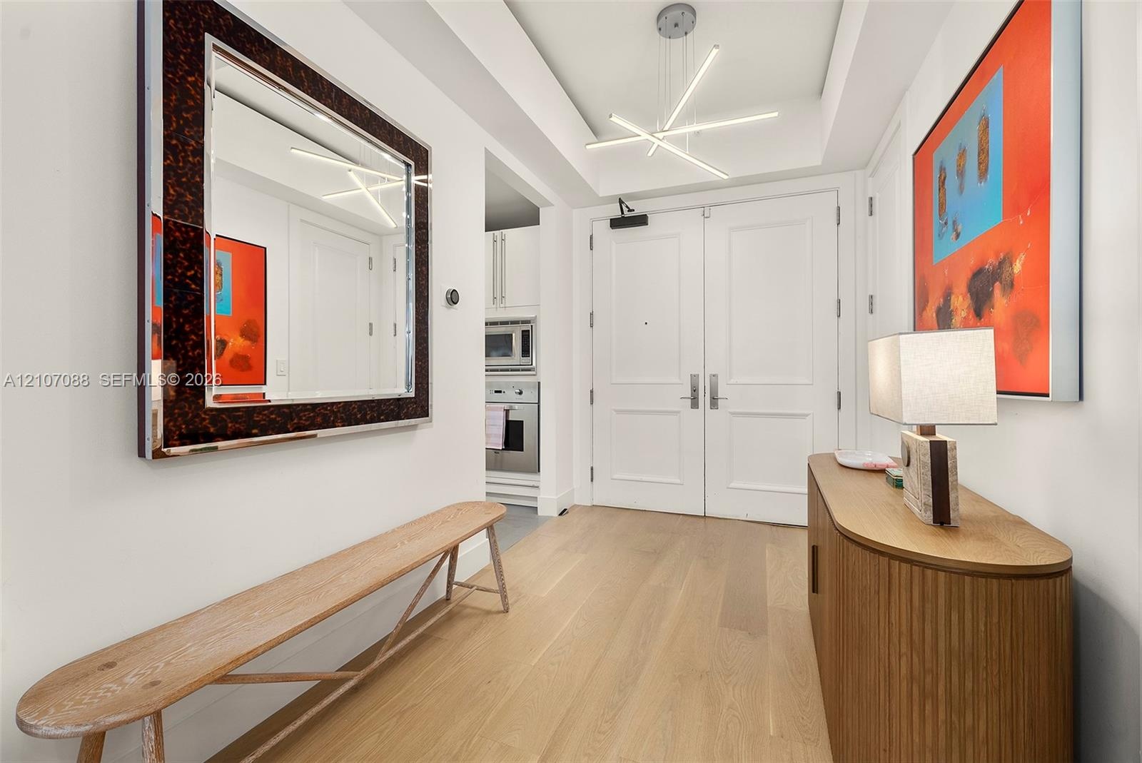 Entryway featuring double doors, wood-finish flooring, a recessed ceiling tray, and a linear geometric light fixture
