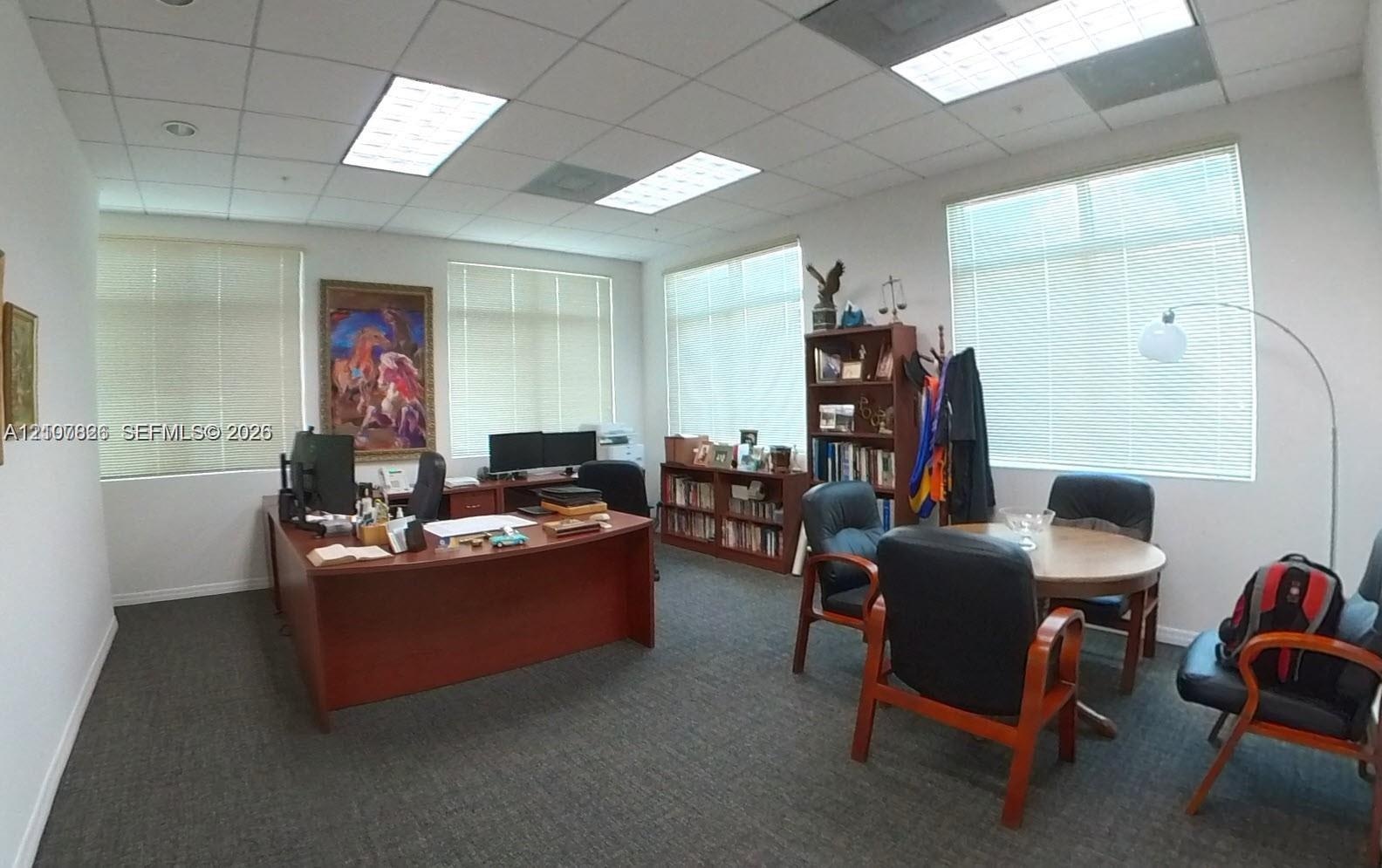 Office interior featuring high-density carpet flooring, recessed fluorescent lighting, and expansive windows with installed blinds