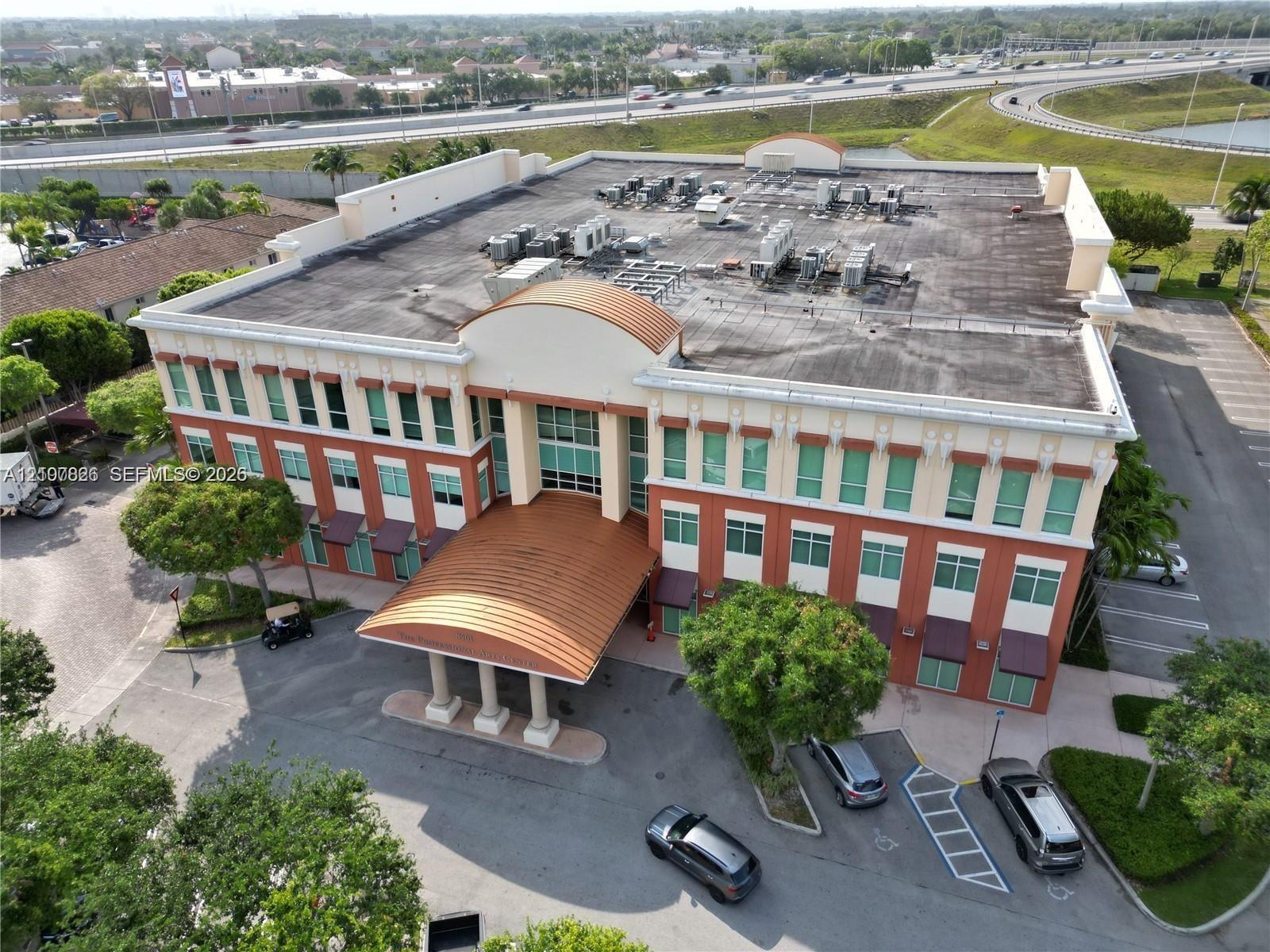 Three-story commercial building featuring a curved metal portico entrance, masonry facade with multi-pane windows, and paved surface parking