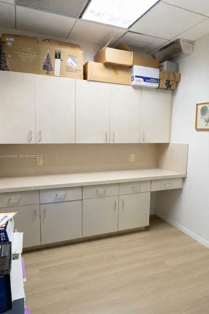 Built-in cabinetry featuring light-toned doors, extensive countertop workspace, wood-finish flooring, and drop-ceiling lighting