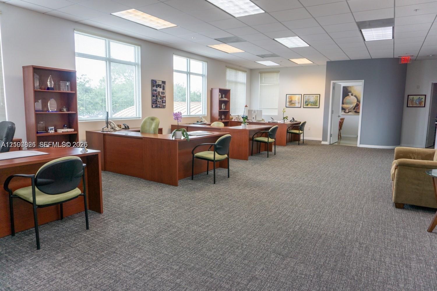 Open-plan interior featuring carpeted flooring, drop ceiling with recessed lighting, and large windows