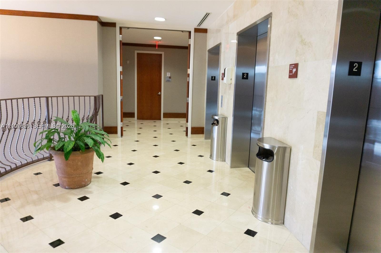 Elevator lobby featuring polished stone flooring with inset accent tiles, stainless steel elevator doors, and neutral wall tiling