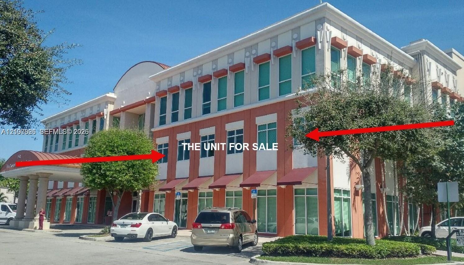 Commercial building exterior featuring a multi-story facade with expansive glass windows, structured red metal awnings, and a covered portico entrance
