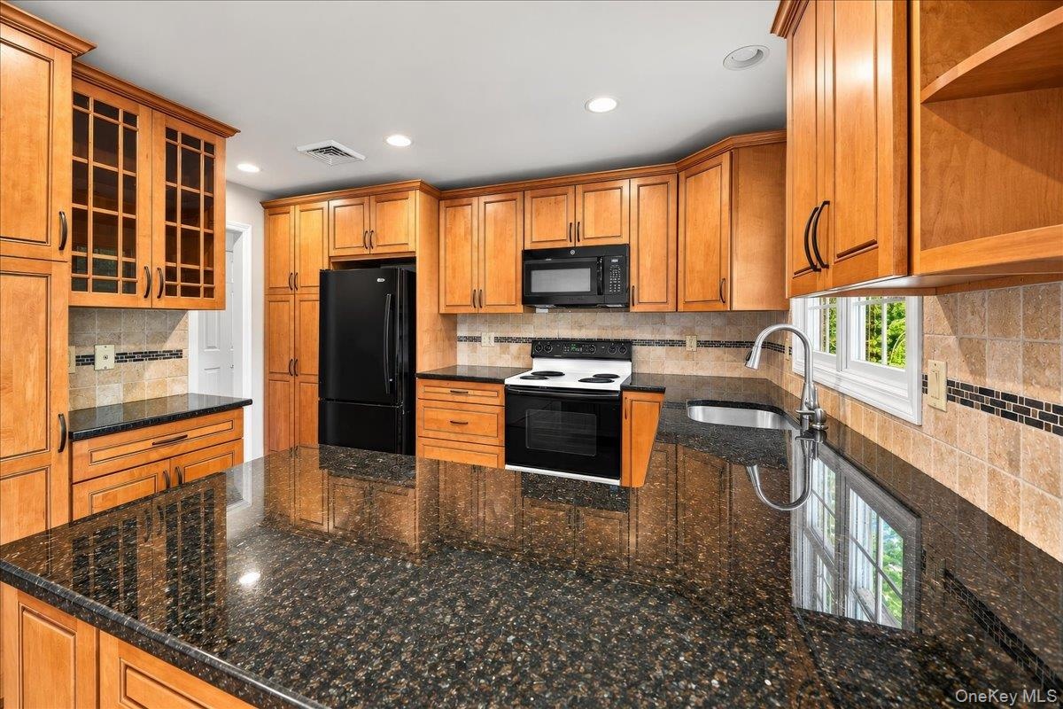 A stylish blend of dark stone countertops, light wood-finish cabinetry, and sleek black built-in appliances creates a modern, inviting kitchen, comple