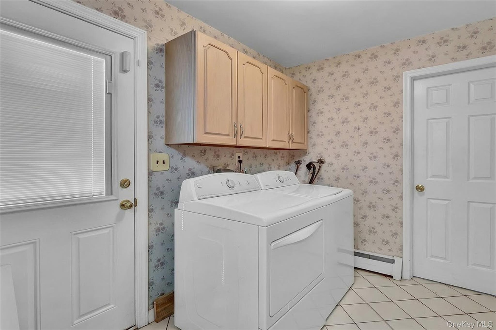Utility space featuring light-toned wood-finish upper cabinetry, tiled flooring, and a six-panel door