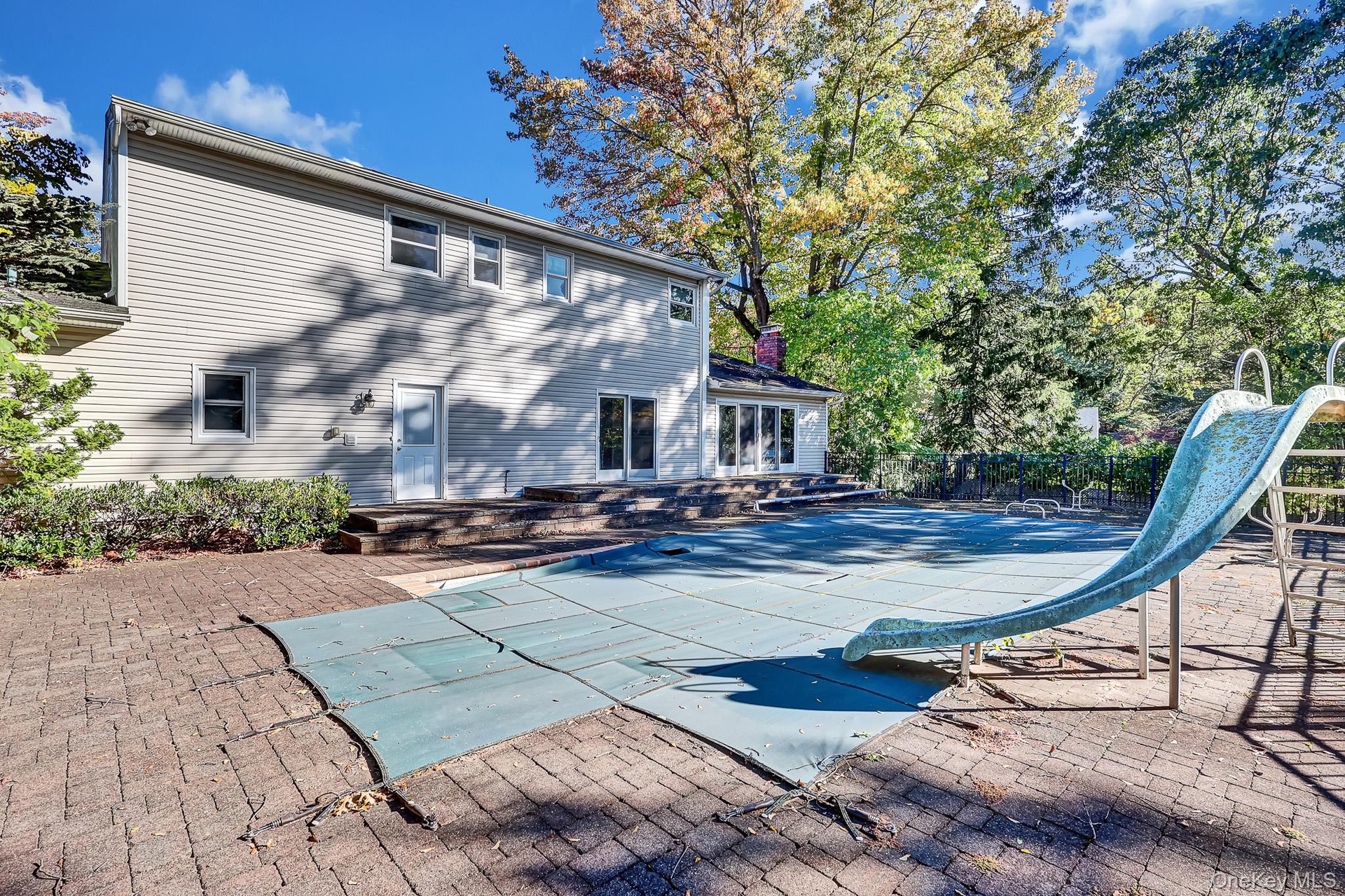 Exterior view of the residence featuring horizontal siding, a multi-level stone paver patio, an in-ground pool with a slide, and mature trees