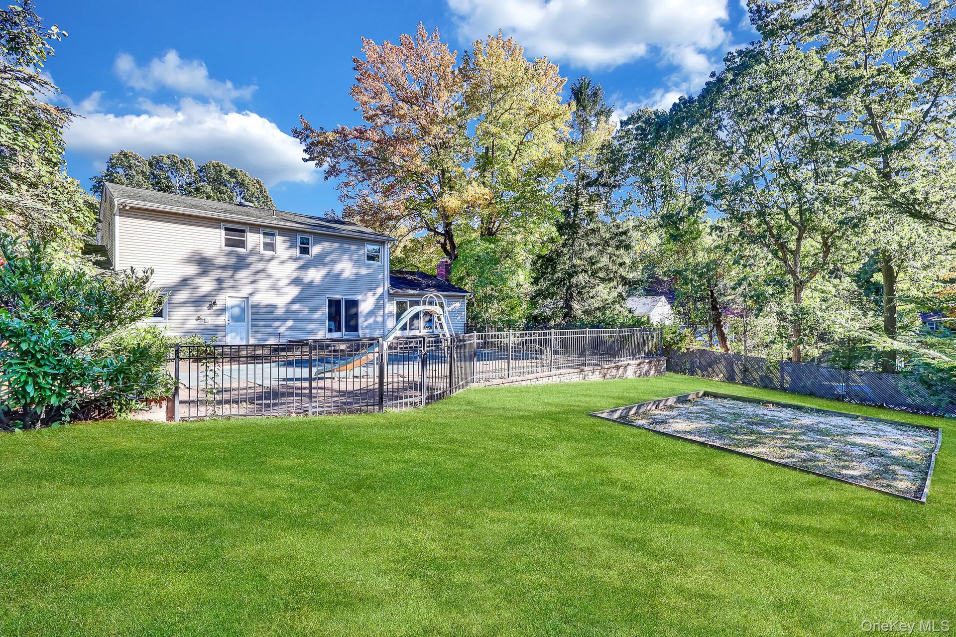 Backyard featuring a manicured lawn, fenced swimming pool with a slide, and a sand area