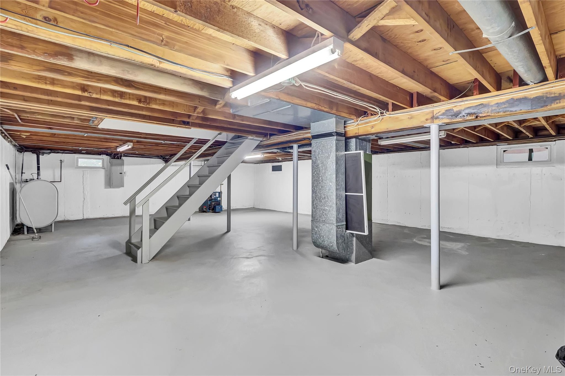 Unfinished lower level featuring exposed wood-beam ceiling construction, painted concrete flooring, structural steel support columns, and interior sta