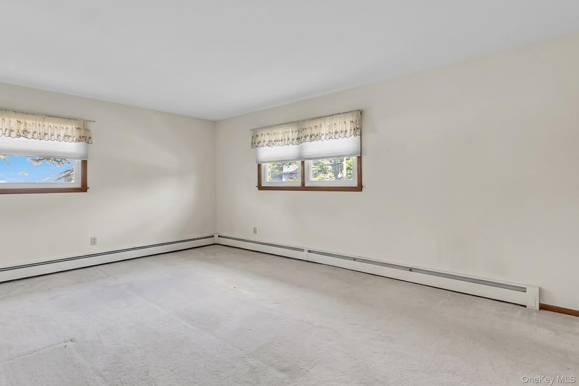 Neutral interior room featuring wall-to-wall carpeting and dual windows with wood-trimmed frames