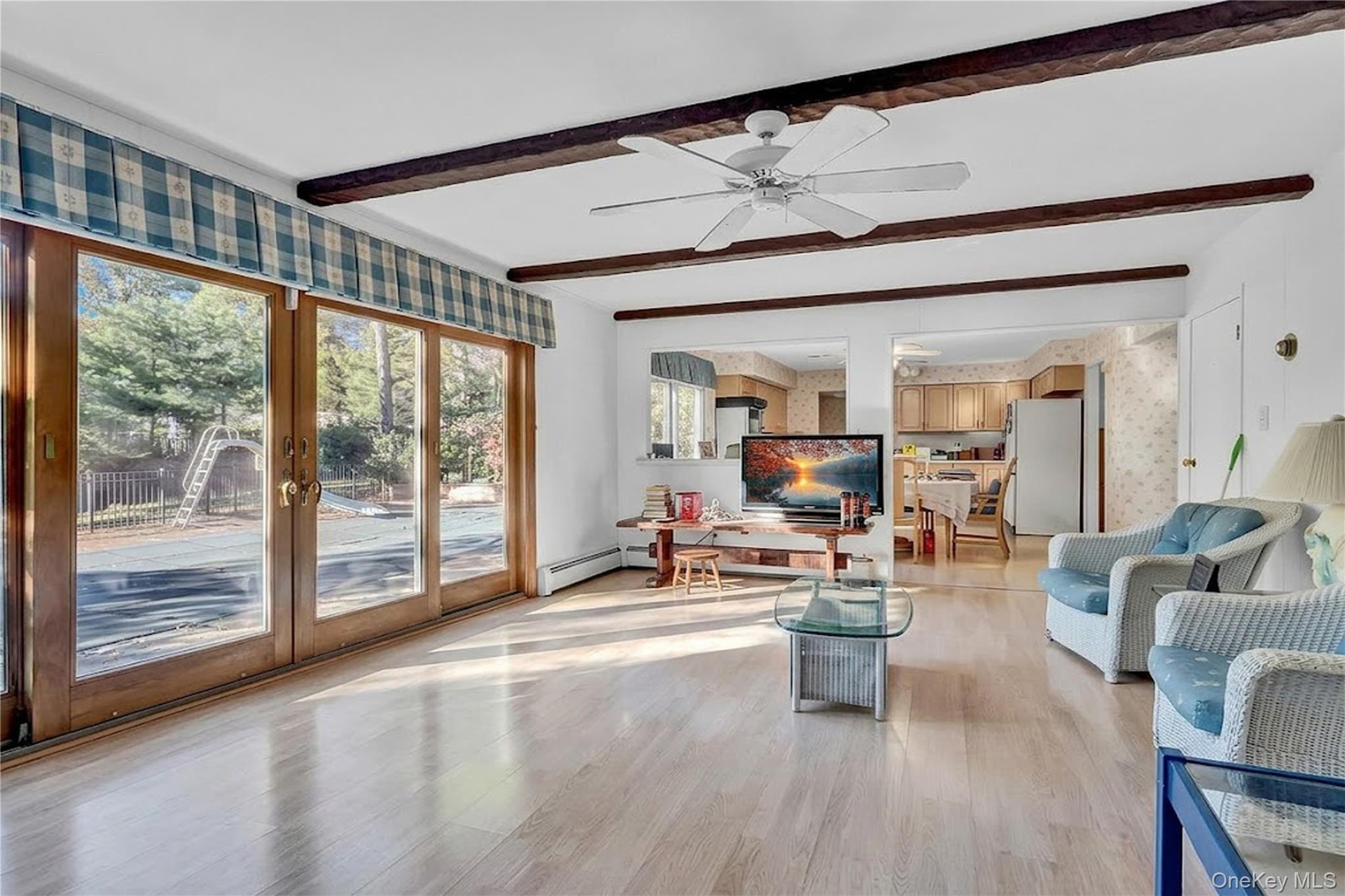 Living space featuring wood-finish flooring, exposed ceiling beams, a ceiling fan, and expansive glass sliding doors