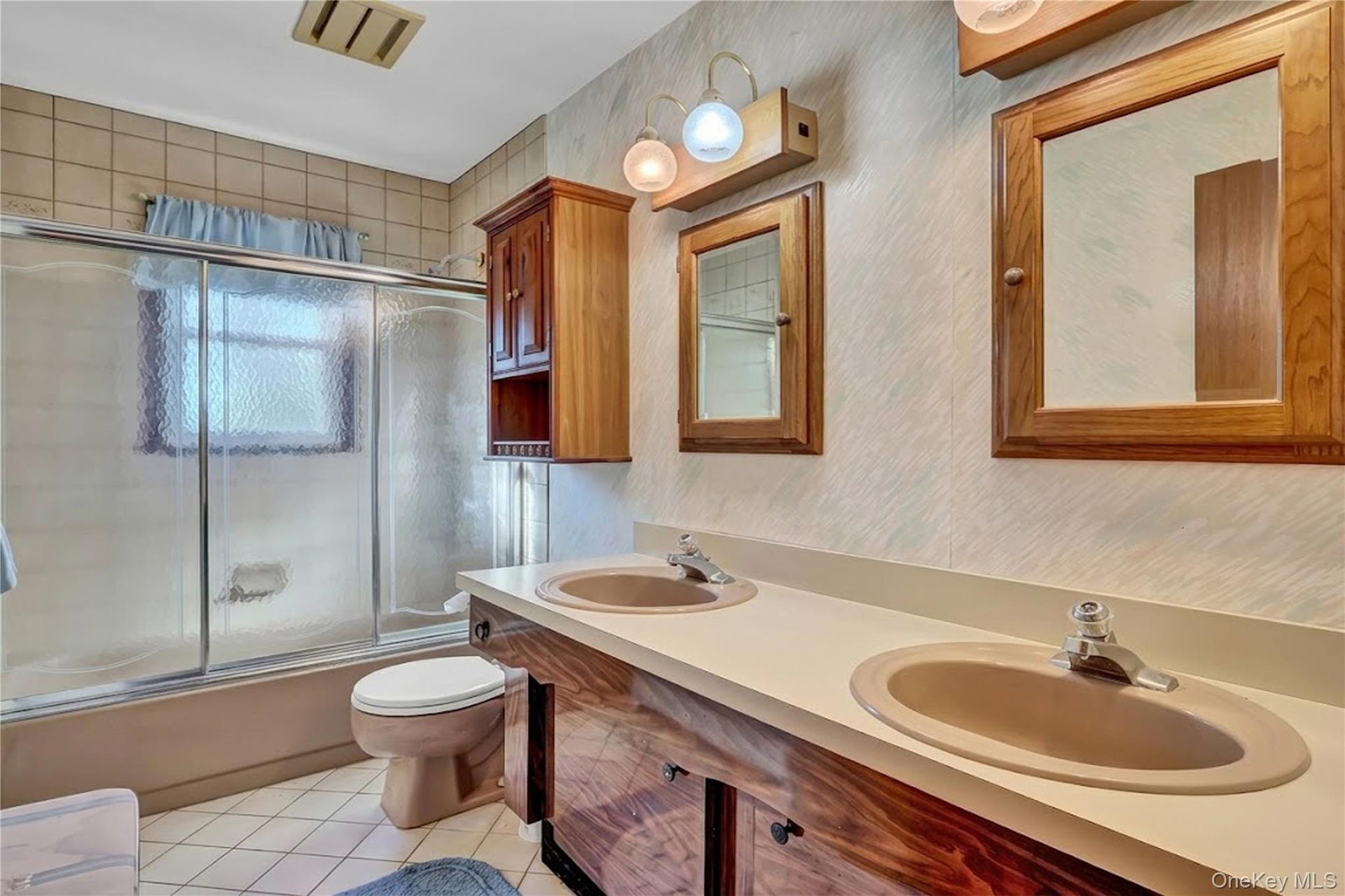 Bathroom featuring a double-sink vanity with wood-finish cabinetry, integrated countertop with dual basins, a glass-enclosed shower and tub combinatio